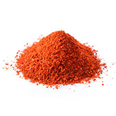En hög med rött pulver av capsicum som ligger på en bänk mot en vit bakgrund