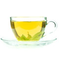 en glaskopp med fat fylld med gront te mot en vit bakgrund