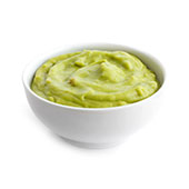 en liten vit skal fylld med ljustgron guacamole mot en vit bakgrund Guacamole
