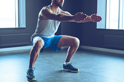 en man i blaa shorts och gratt linne gor knaboj, squats