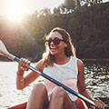 en skrattande kvinna i solglasogon paddlar kajak i en sjo, i solnedgangen