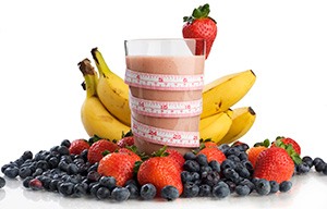 Ett glas med smoothie star i en hog jordgubbar, blabar och bananer. Ett mattband runt glaset. mot vit bakgrund