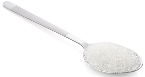 en vit sked som ar fylld med socker, mot en vit bakgrund