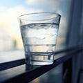 ett glas vatten med is balanserar på en fonsterkarm i motljus